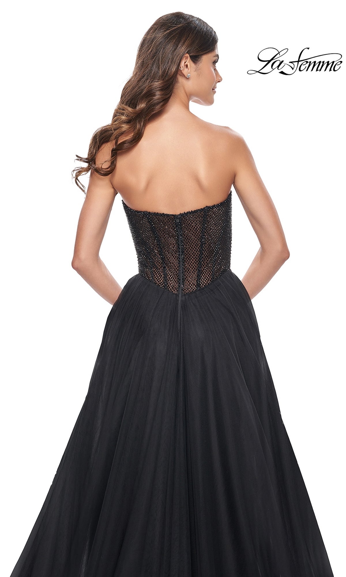 A woman models the La Femme Strapless Long A-Line Prom Dress 32216, featuring a fitted textured bodice and full tulle skirt, shown from the back against a white background. This elegant formal gown offers timeless sophistication.